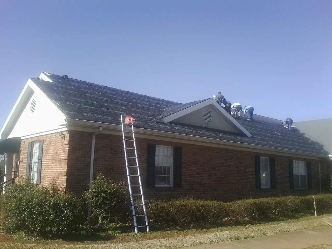 Crew tearing shingles off a brick ranch roof with a ladder set — Emergency Roof Repair work by our crew in Notre Dame