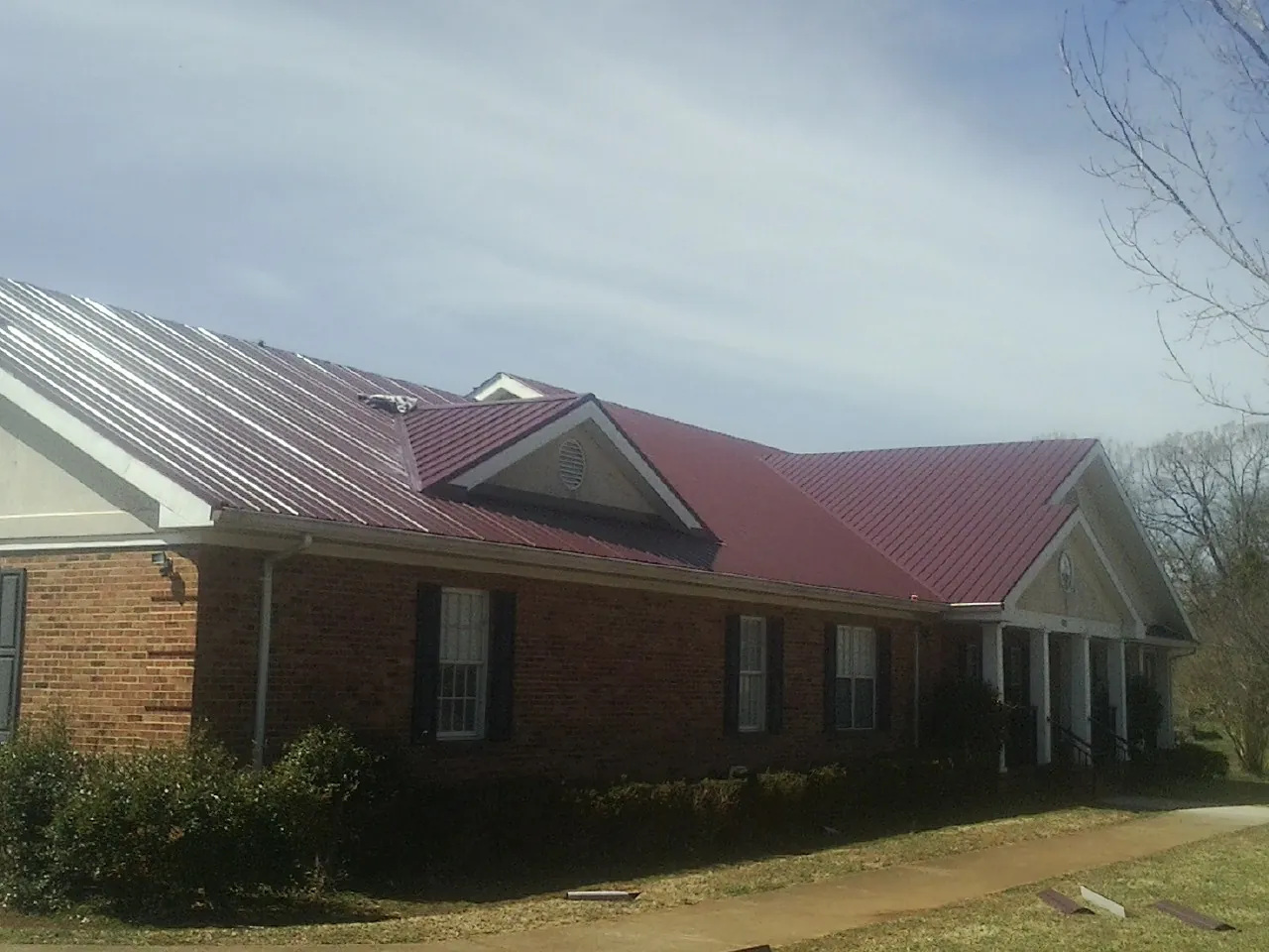 Red metal roof with gabled entries on a long brick building, from a Hail Damage Roof Repair job in Notre Dame