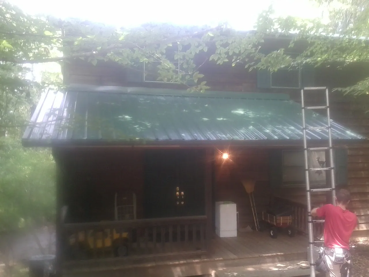 Worker on a ladder at the green porch roof of a wooded cabin in Notre Dame