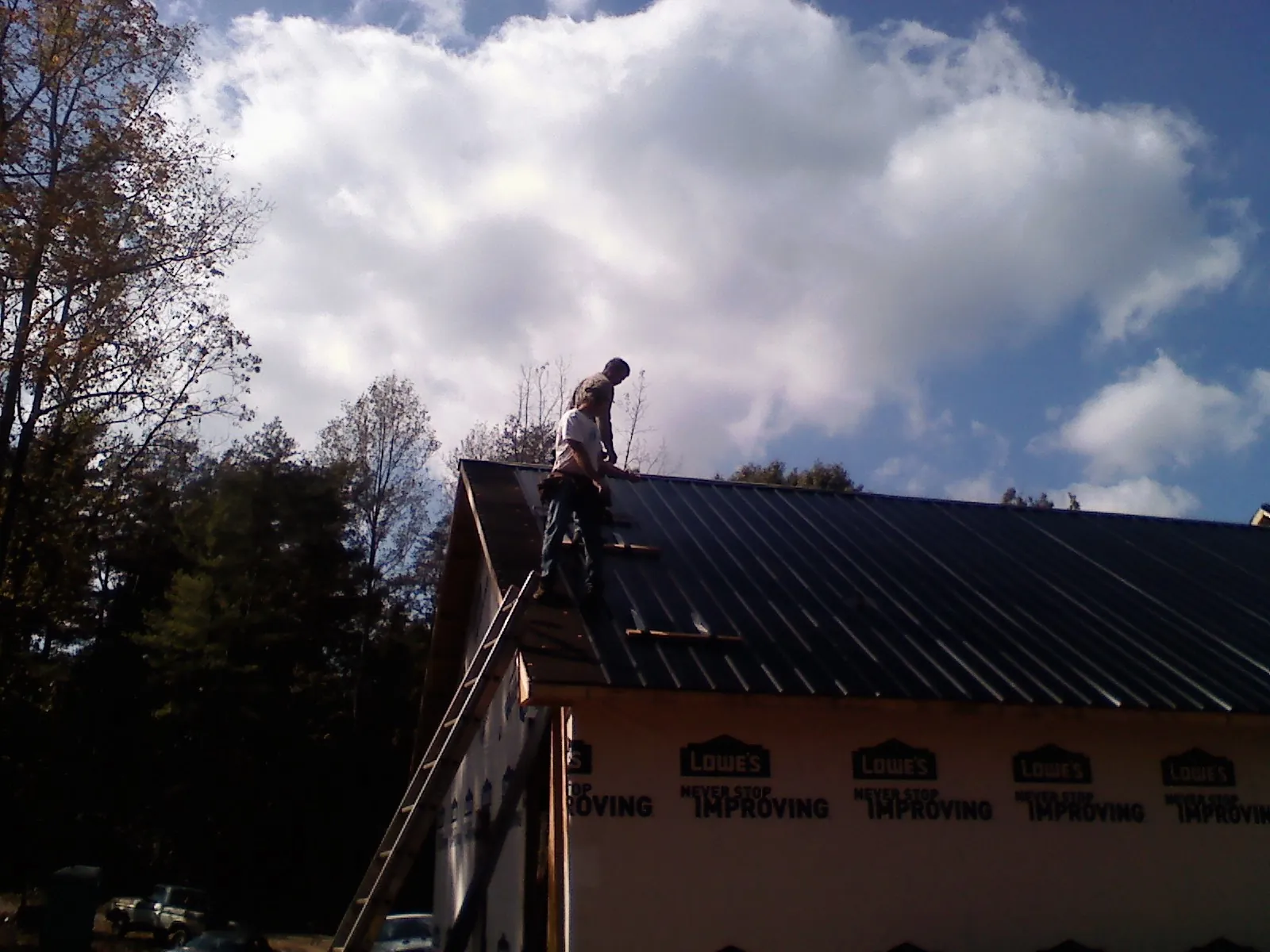 Roofer fastening dark metal panels high against a cloudy sky, from a Roof Inspection job in Notre Dame