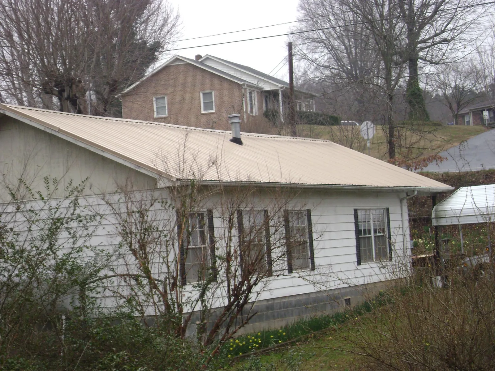 Tan metal roof on a white sided house set into a hillside — Commercial Roofing by Roofing Brothers in Notre Dame