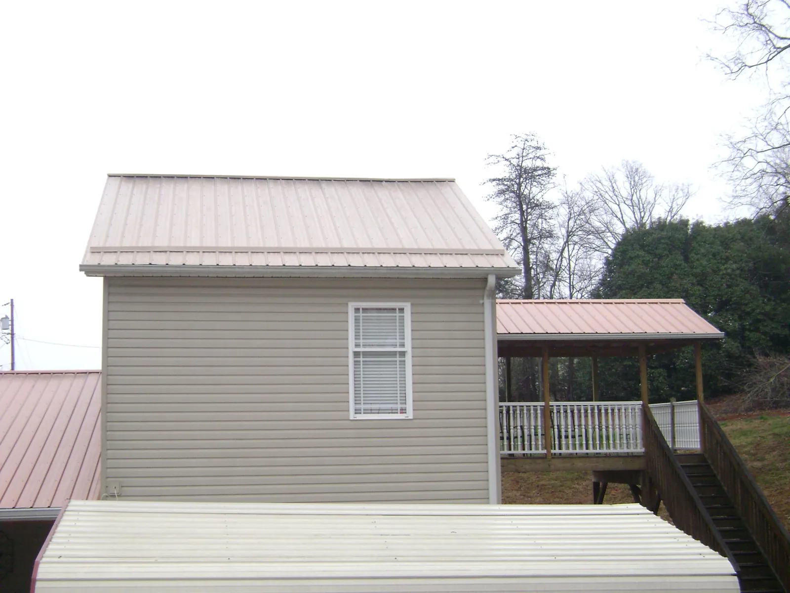 Tan metal roofs on a two story addition and attached porch, from a Roof Replacement job in Notre Dame